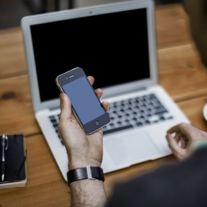 Man looking at his phone while sitting with a laptop in front of him